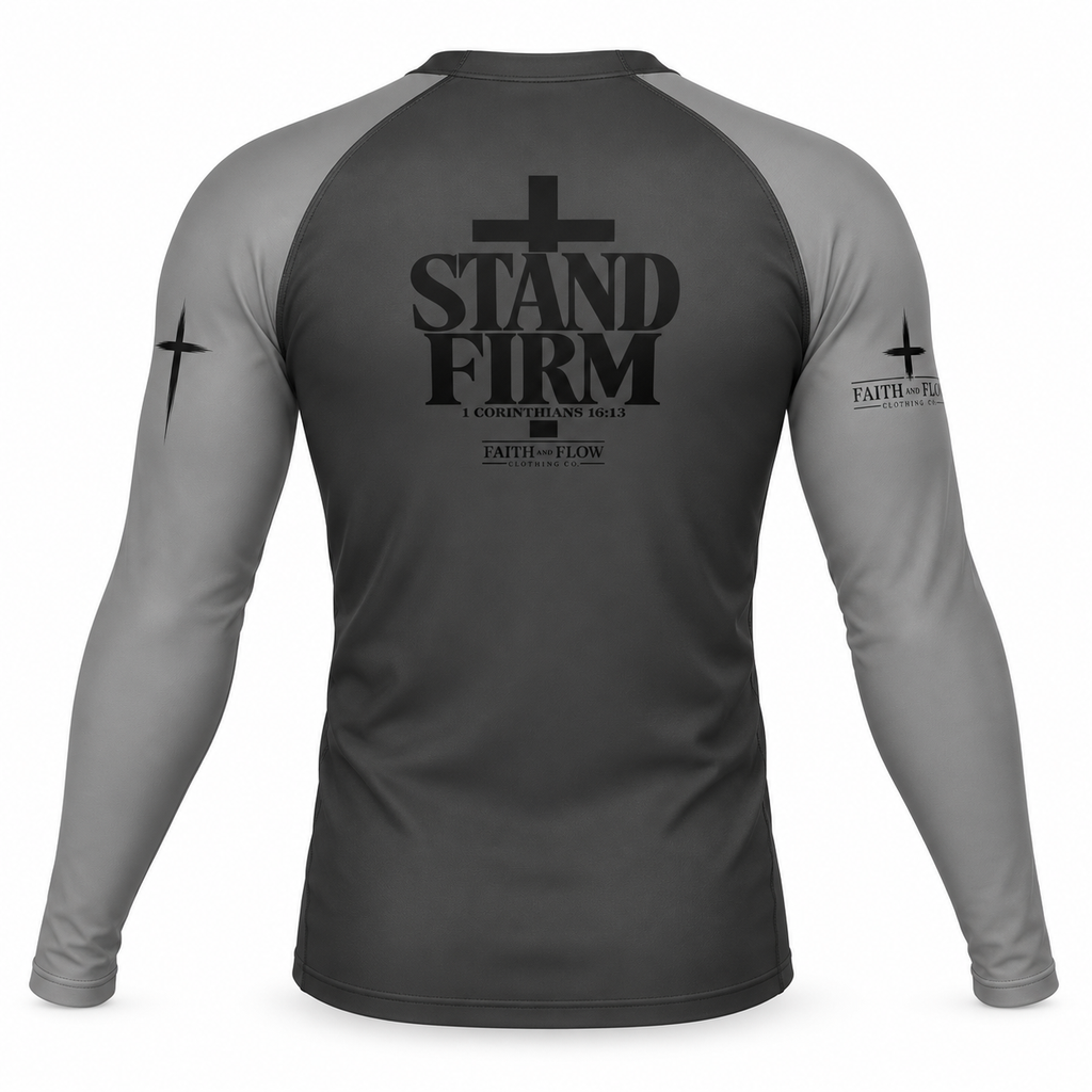 A long-sleeve athletic rash guard shown from the back, featuring a dark gray body and lighter gray sleeves. The back has a large black graphic with a cross and the text 'STAND FIRM', with smaller text below and a cross graphic on each sleeve.