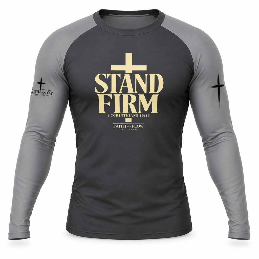 A long-sleeve raglan t-shirt in dark gray and medium gray, featuring a gold graphic on the chest that reads 'STAND FIRM' with a cross above it, and 'FAITH - FLOW' printed on the sleeve.